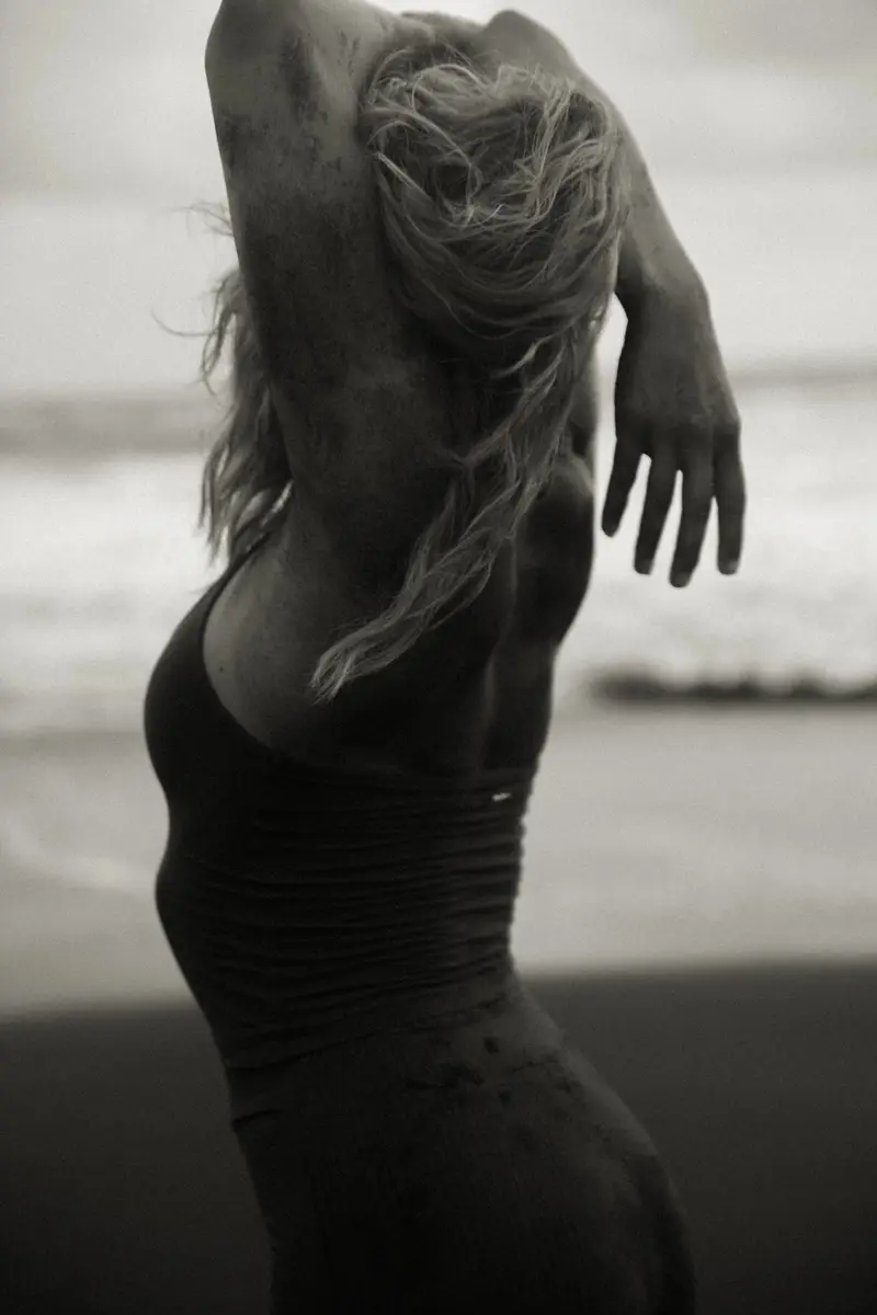 Femme de dos en maillot, les bras levés dans les cheveux, en noir et blanc
