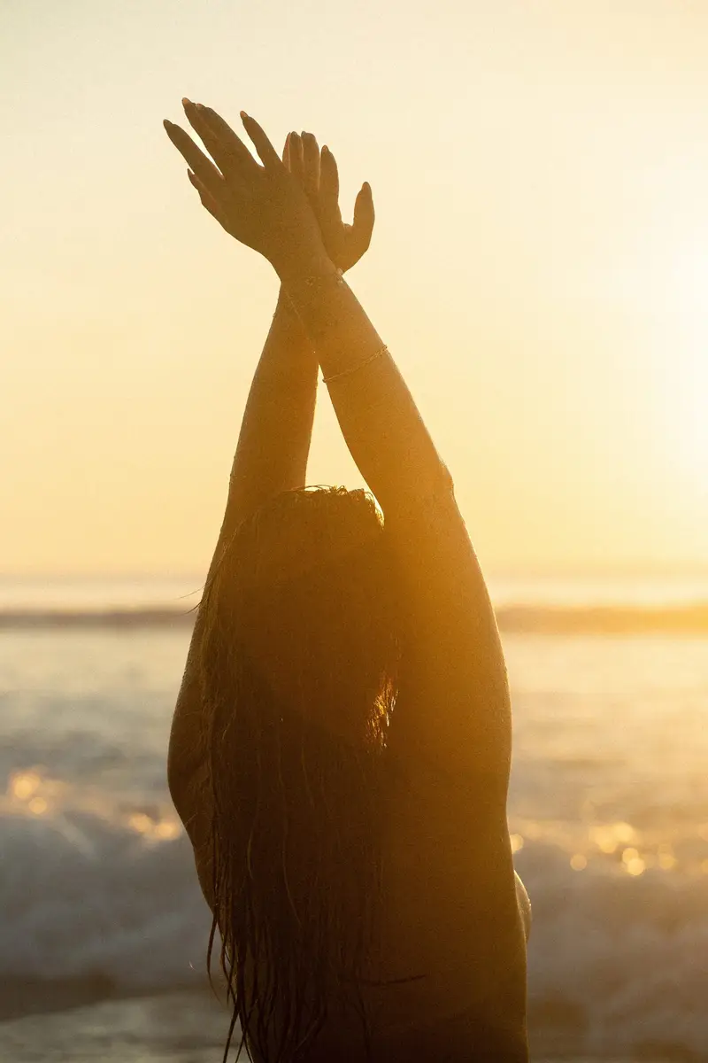 Silhouette les bras levés face au soleil couchant, au bord de l'océan