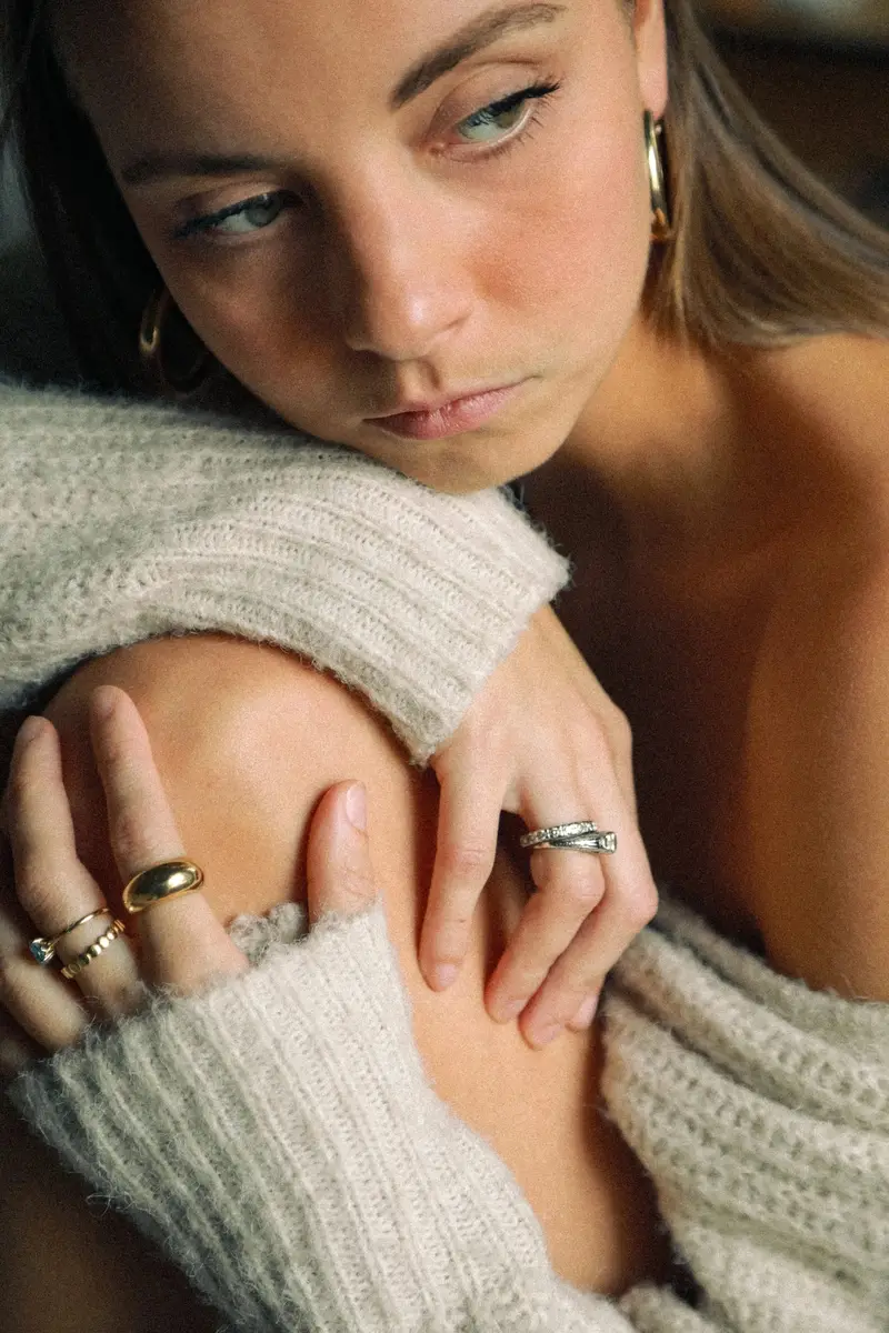 Femme en pull crème, la tête posée sur ses bras, des bagues aux doigts