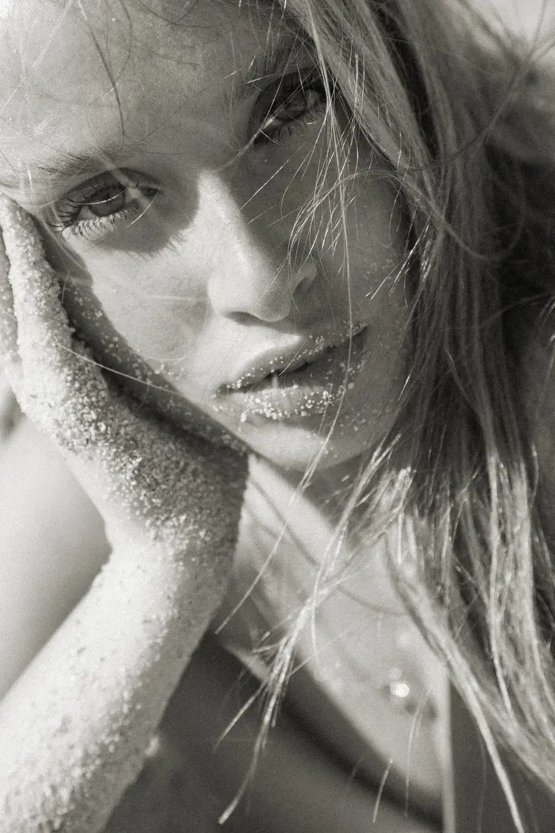 Portrait en noir et blanc d'une femme, le visage entre ses mains couvertes de sable